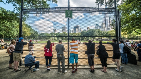 baseball field in Central Park with people watching through fence behind home plate on summer day