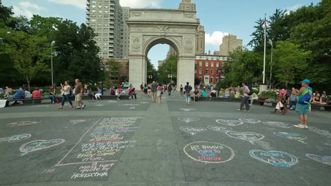 chalk art and writing on ground in Washington Square Park with arch and people on summer day in NYC