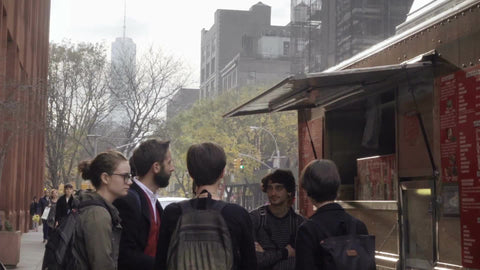NYU students in group, talking by Halal Guys food truck with Freedom Tower in background in fall, New York City