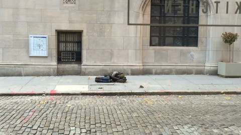 homeless man curled up sleeping on sidewalk in front of church on cold winter day, view from restaurant in New York City