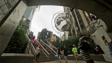 Columbus Circle subway station with Steel Globe sculpture and people walking down stairs on summer day in NYC