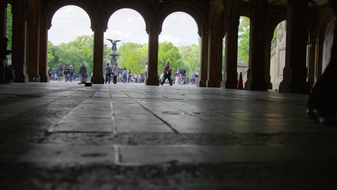 silhouette of feet walking on ground under Bethesda Terrace in Central Park in slow motion with statue