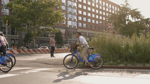 hipster on Citi Bike and yellow taxi cab driving in Greenwich Village on sunny day in summer