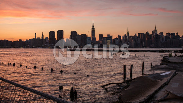Manhattan skyline with Empire State Building silhouette view from Brooklyn across East River with wood dowels in water - early evening pink orange and purple sunset in NYC
