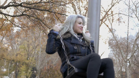 beautiful woman playing on swing in Central Park on cold fall day - pretty girl swinging in slow motion