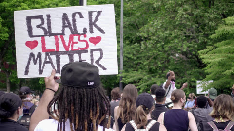 Black Lives Matter sign in crowd at BLM rally in Washington Square Park with leader speaking in background in New York City