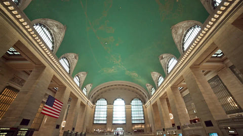 tilting down from Grand Central Station ceiling to stairs below with people in crowded room in summer NYC