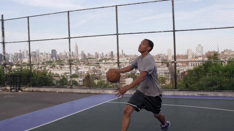 kid jumping up scoring layup on basketball court with view of Manhattan skyline through fence
