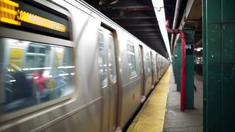 subway train leaving West 4th Street station with woman leaning on column on platform
