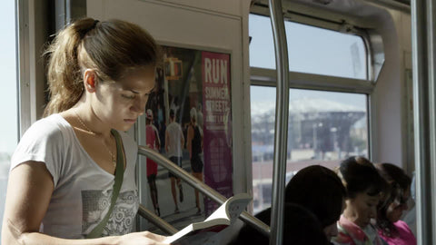 beautiful sporty woman reading on elevated subway train, standing in summer
