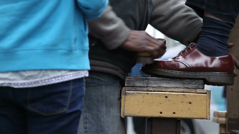 shoe shiner shining red brown shoes during day in close-up, NYC