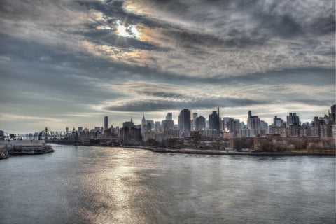 Manhattan skyline from across East River in late afternoon early evening - sun beaming through clouds onto water in HDR
