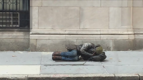 homeless man curled up cold on the street sleeping on sidewalk