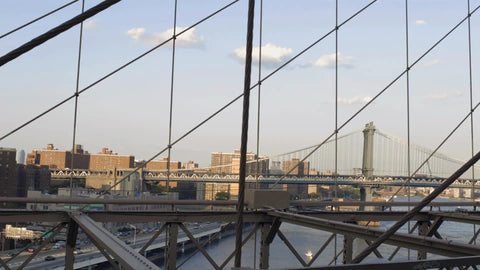 tourists crossing Brooklyn Bridge with view of Manhattan Bridge and East River in summer NYC