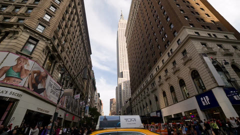 driving past Herald Square with view of Empire State Building through buildings on sunny summer day