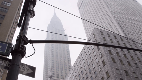 Chrysler Building in Midtown Manhattan with people crossing street on foggy day - upward angle of tall skyscraper in 4K NYC