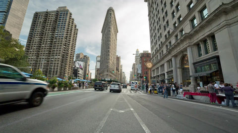 cars and cabs driving down Lower 5th Ave on summer day with Flatiron Building