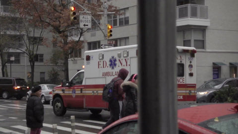 FDNY emergency ambulance truck driving down street on rainy day - view from under scaffolding