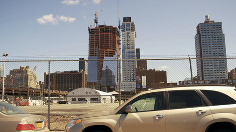 cars driving along Westside Highway past fence and construction site with developments - 4K in Manhattan NYC