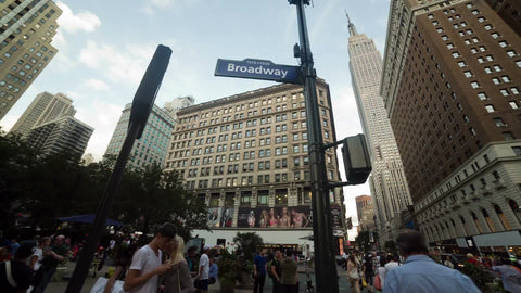 panning across crowded street and Broadway sign in Herald Square with Empire State Building towering overhead on summer day in NYC