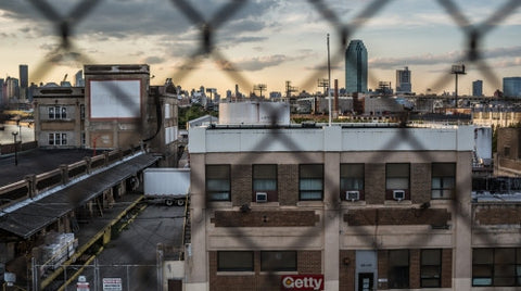 gritty view of Brooklyn through fence at sunset with Manhattan buildings and skyscrapers in background in NYC