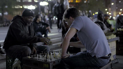 old black man and young white kid playing chess outside in Union Square at night in NYC
