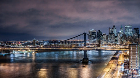 Manhattan Bridge and East River water with motion blurred cars as streaks of light on the FDR Drive highway at night in NYC