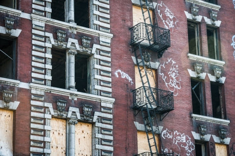 abandoned tenement with fire escapes - boarded up windows - gritty graffiti on red building in ghetto