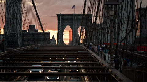 cars driving in slow traffic on Brooklyn Bridge with American flag at sunset in early evening in NYC