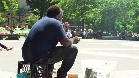 man sitting on a milk crate smoking cigarette in Washington Square Park on hot summer day in NYC