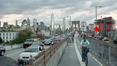 cars and bicycles exiting Brooklyn Bridge with view of Manhattan skyline in distance in summer late afternoon in NYC