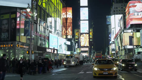 taxi cab driving through Times Square at night with bright lights and billboards in NYC