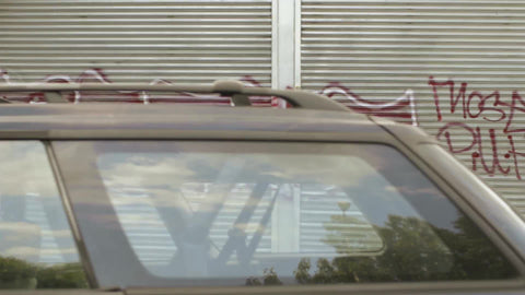 gritty graffiti on wall, metal gate, and building on sunny day in Brooklyn - driving shot