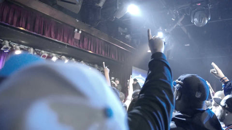 big crowd at hip hop show under bright lights - fans facing stage with hands in the air - slow motion