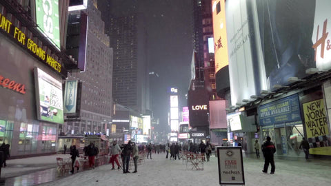 couple in Times Square night - snowing with tourists looking up and pointing at bright lights in New York City