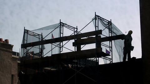construction worker in hardhat working on building scaffolding on summer day - silhouette of man working in NYC