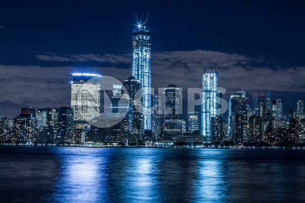 Downtown Manhattan skyline with Freedom Tower and skyscrapers at night reflections off East River water