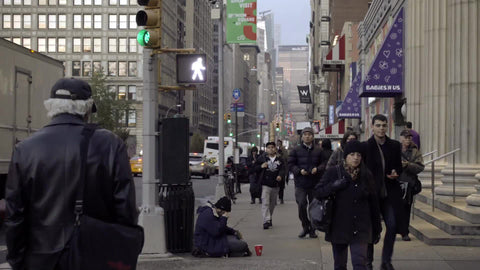 homeless man sitting on street - tragic scene on Park Avenue with people walking by in winter