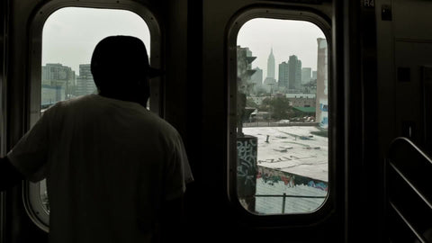 silhouette of man in baseball cap riding elevated subway train in Queens in NYC