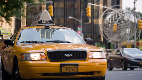 taxi driving off from Columbus Circle on summer day with taxicab stand and steel globe sculpture in background in Manhattan NYC