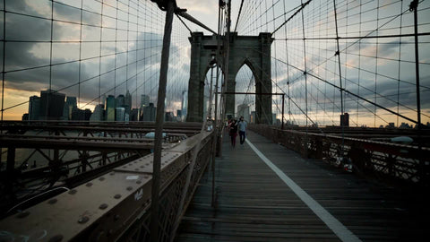 people crossing Brooklyn Bridge at sunset in early evening in summer in NYC