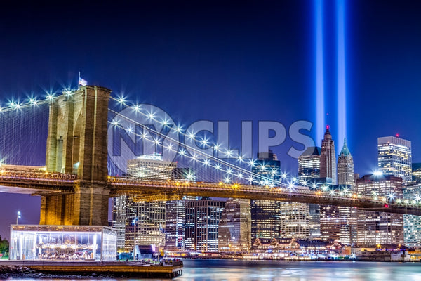 911 memorial lights, beams over Manhattan skyline with buildings and skyscrapers and Brooklyn Bridge lit up at night - carousel on East River