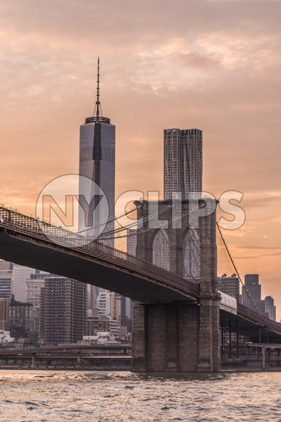 Freedom Tower and 8 Spruce Street with Brooklyn Bridge at sunset across East River water in NYC