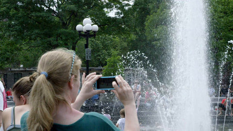 woman taking picture with smartphone of children in Washington Square Park circle fountain in slow motion in summer - 4K NYC