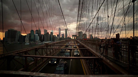 wide shot over cars driving in traffic on Brooklyn Bridge at beautiful sunset with Manhattan skyline in background in early evening in NYC