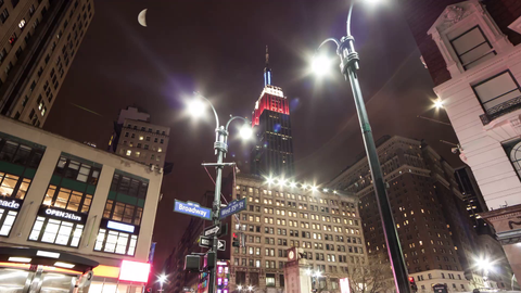 Herald Square 35th street and Broadway corner with red white and blue Empire State Building overhead and moon at night in 4k timelapse in NYC