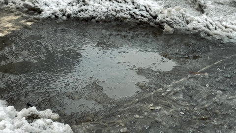 man in boots stepping over and avoiding ice puddle with snow and slush in cold wet winter
