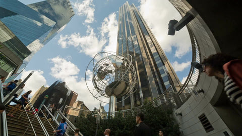 people exiting Columbus Circle subway station by stairs with globe sculpture and Trump Tower overhead on summer day in NYC