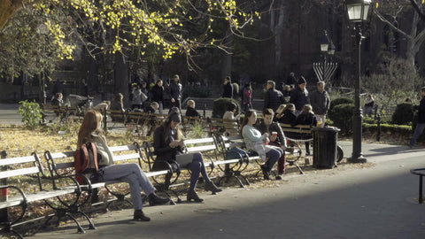 people on Washington Square Park benches in autumn with menorah and trees Fall in New York City