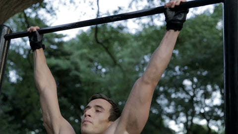 muscular man doing pull-ups in Central Park - athletic gymnast doing gymnastics on bar